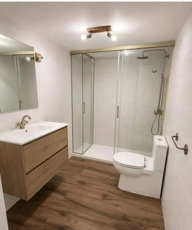 Baño con ducha de doble puerta, griferia dorada y suelo imitación madera