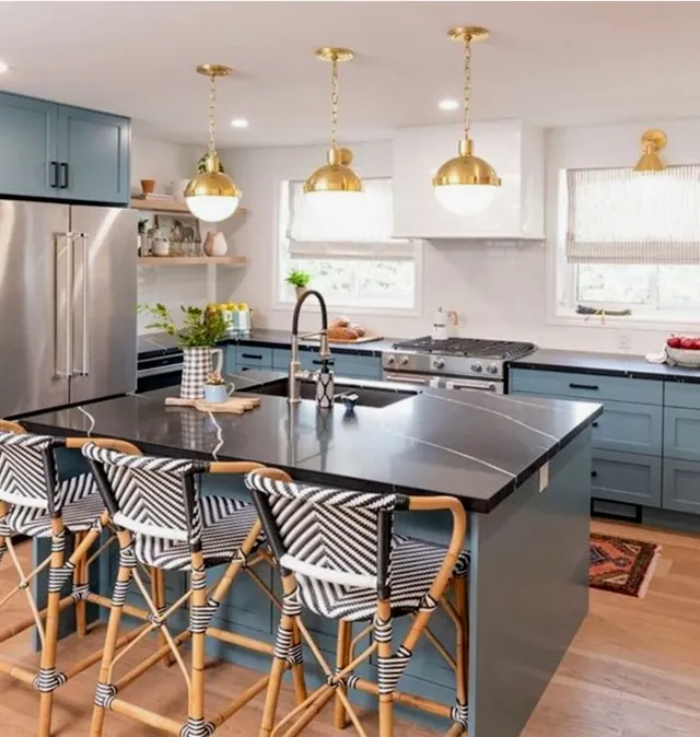 Cocina en azul con isla central, encimera oscura y lámparas doradas colgantes