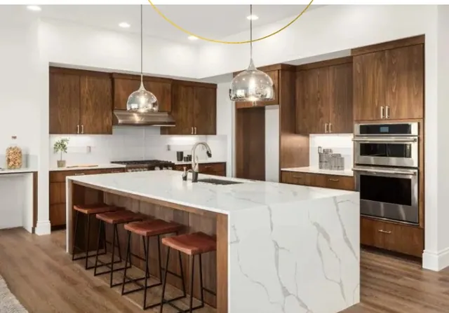 Cocina con muebles en madera oscura, isla con encimera de mármol y electrodomésticos integrados