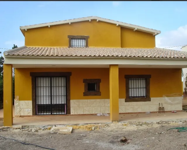 Fachada de una vivienda unifamiliar en obra, con revestimiento ocre y huecos de ventana sin terminar