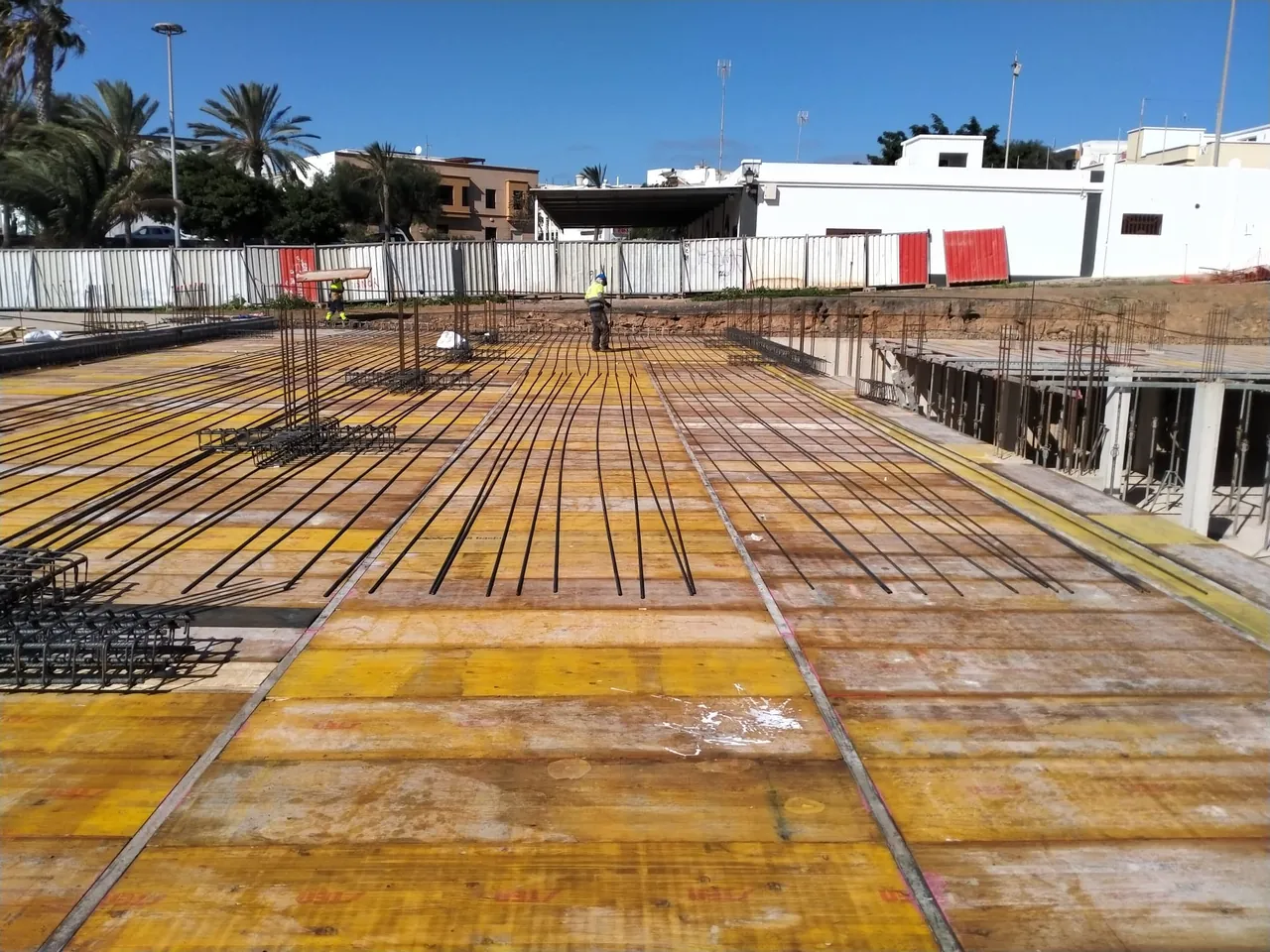Forjado encofrado con tableros amarillos y la ferralla de los nervios colocada, con operarios trabajando al fondo