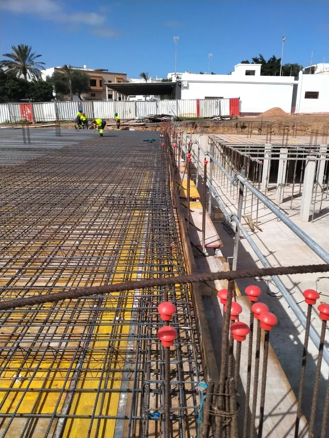 Forjado con mallazo sobre encofrado amarillo y esperas de pilares con tapones rojos en primer plano