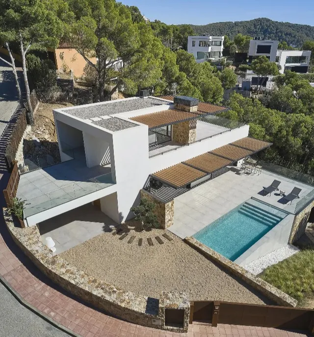 Vista aérea de una vivienda moderna con piscina y terraza de piedra entre vegetación